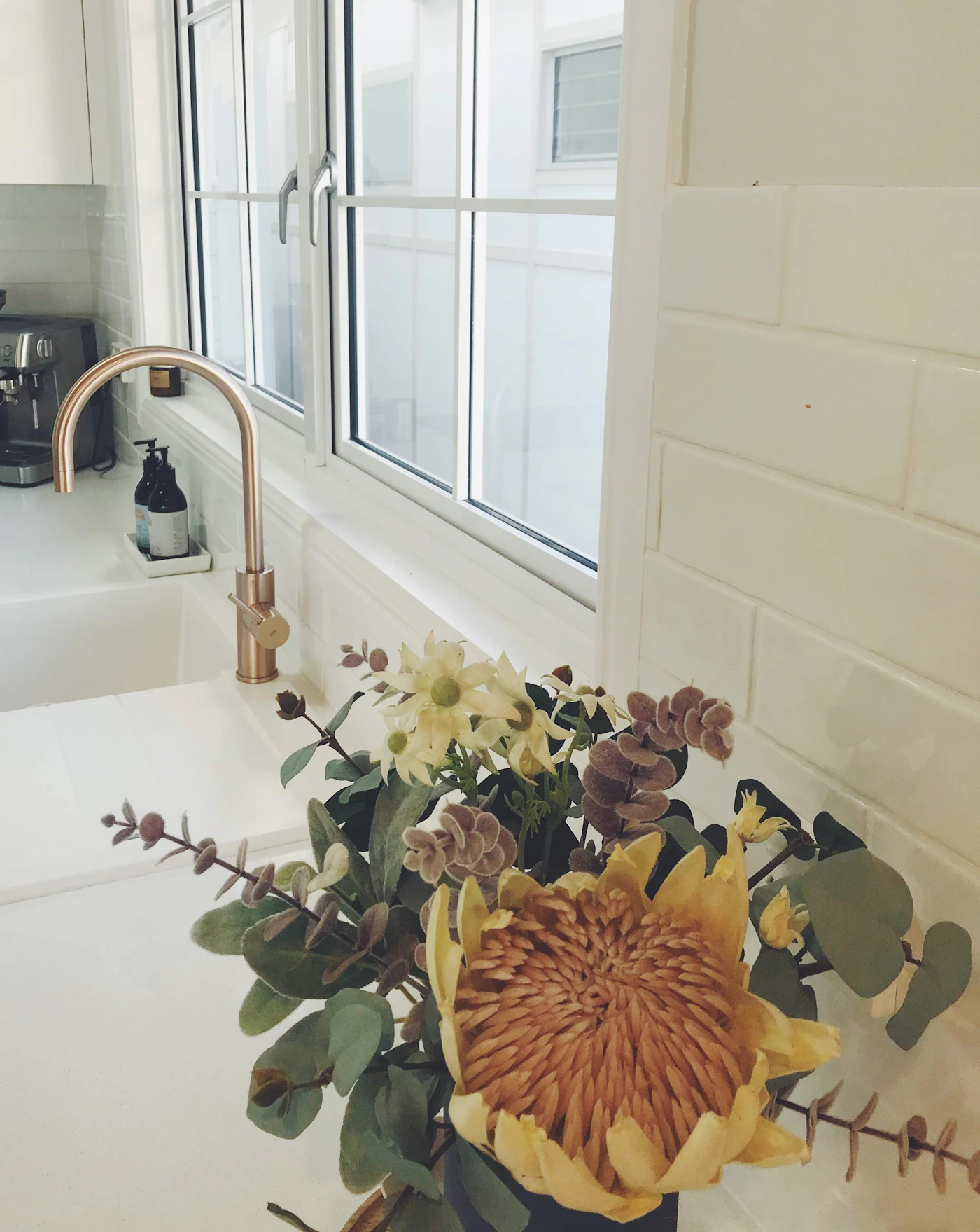 Single orange flower in a vase positioned beside a clean white sink and faucet