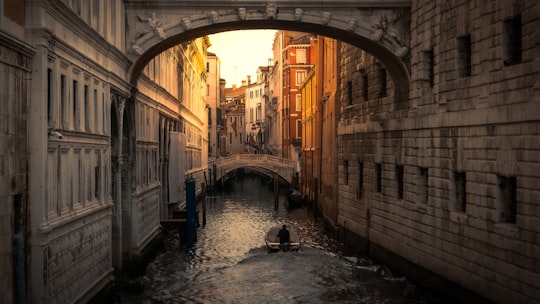 people riding on boat on river between brown concrete buildings during daytime in Bridge of Sighs Italy