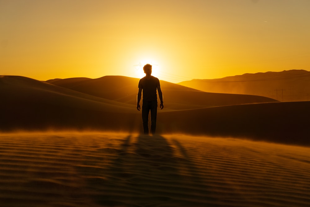 man in black jacket standing on brown sand during sunset