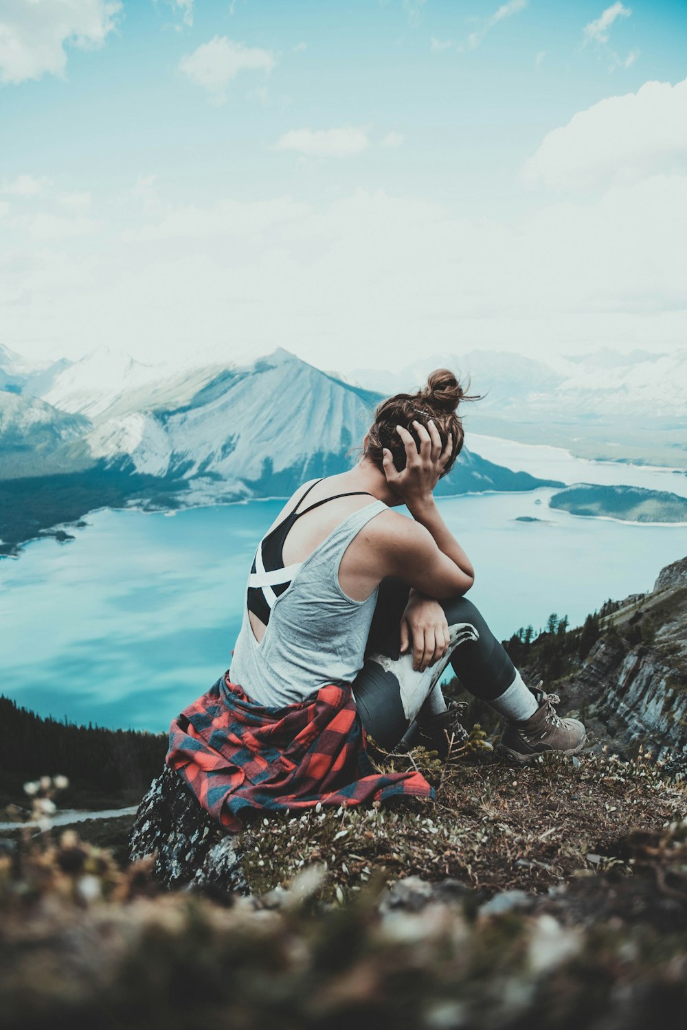 woman in white tank top and red skirt sitting on rock near lake during daytime