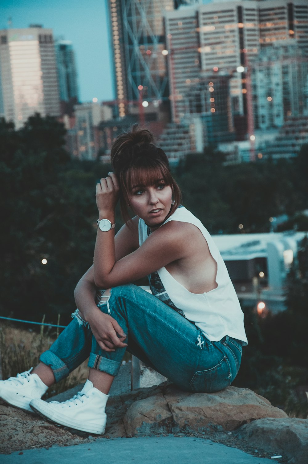 woman in white tank top and blue denim jeans sitting on brown wooden fence during daytime