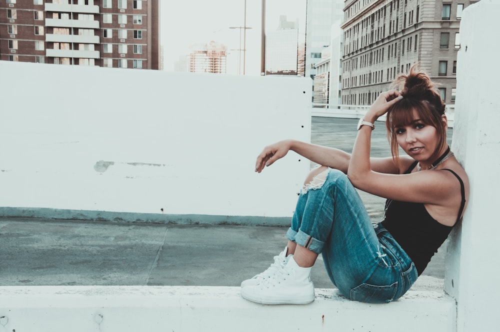 woman in blue denim jeans and white sneakers sitting on white concrete wall during daytime