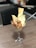 A glass goblet is filled with a culinary dish, featuring chunks of golden-brown crispy chicken topped with garnish, accompanied by large, thin pieces of seasoned flatbread. A spoon is placed in the goblet, and it rests on a wooden dining surface with a blurred background.