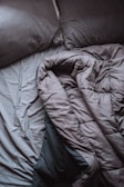 A pair of crumpled, gray bed sheets and pillows create a relaxed, unmade appearance. The rumpled bedding suggests hint of recent use, and the soft texture is visible in its folds.