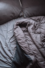 A pair of crumpled, gray bed sheets and pillows create a relaxed, unmade appearance. The rumpled bedding suggests hint of recent use, and the soft texture is visible in its folds.