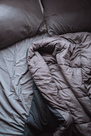 A pair of crumpled, gray bed sheets and pillows create a relaxed, unmade appearance. The rumpled bedding suggests hint of recent use, and the soft texture is visible in its folds.