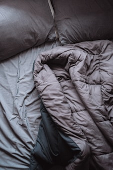 A pair of crumpled, gray bed sheets and pillows create a relaxed, unmade appearance. The rumpled bedding suggests hint of recent use, and the soft texture is visible in its folds.