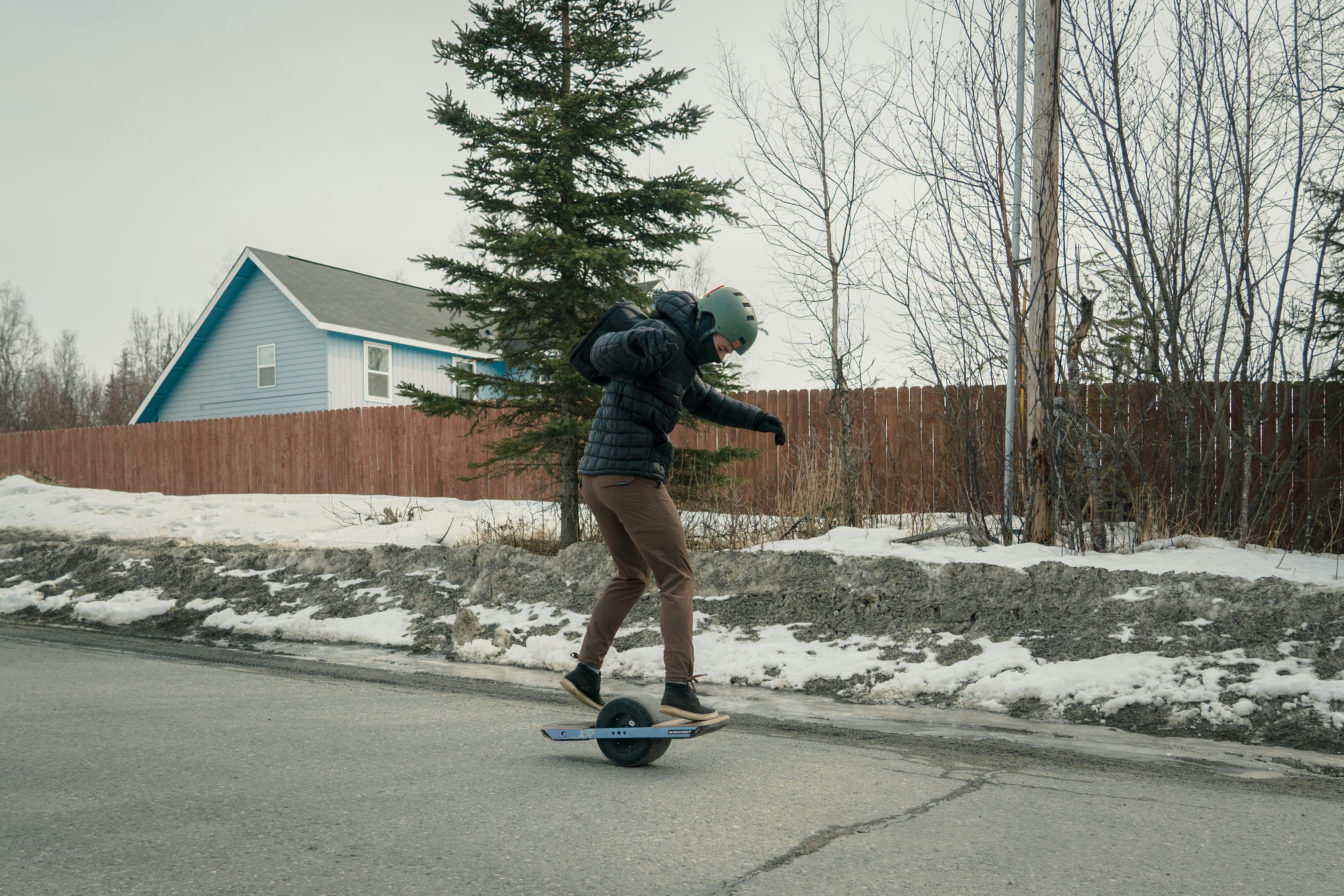 man in black jacket and blue denim jeans riding blue skateboard on gray concrete road during