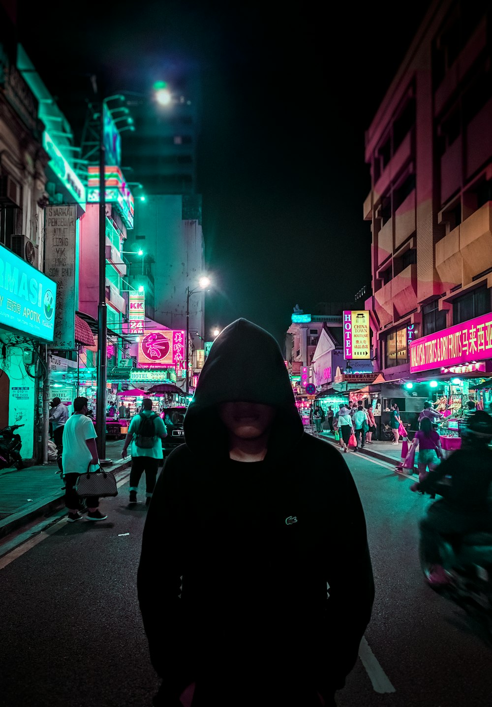 Mann in schwarzem Kapuzenpulli geht nachts auf der Straße spazieren