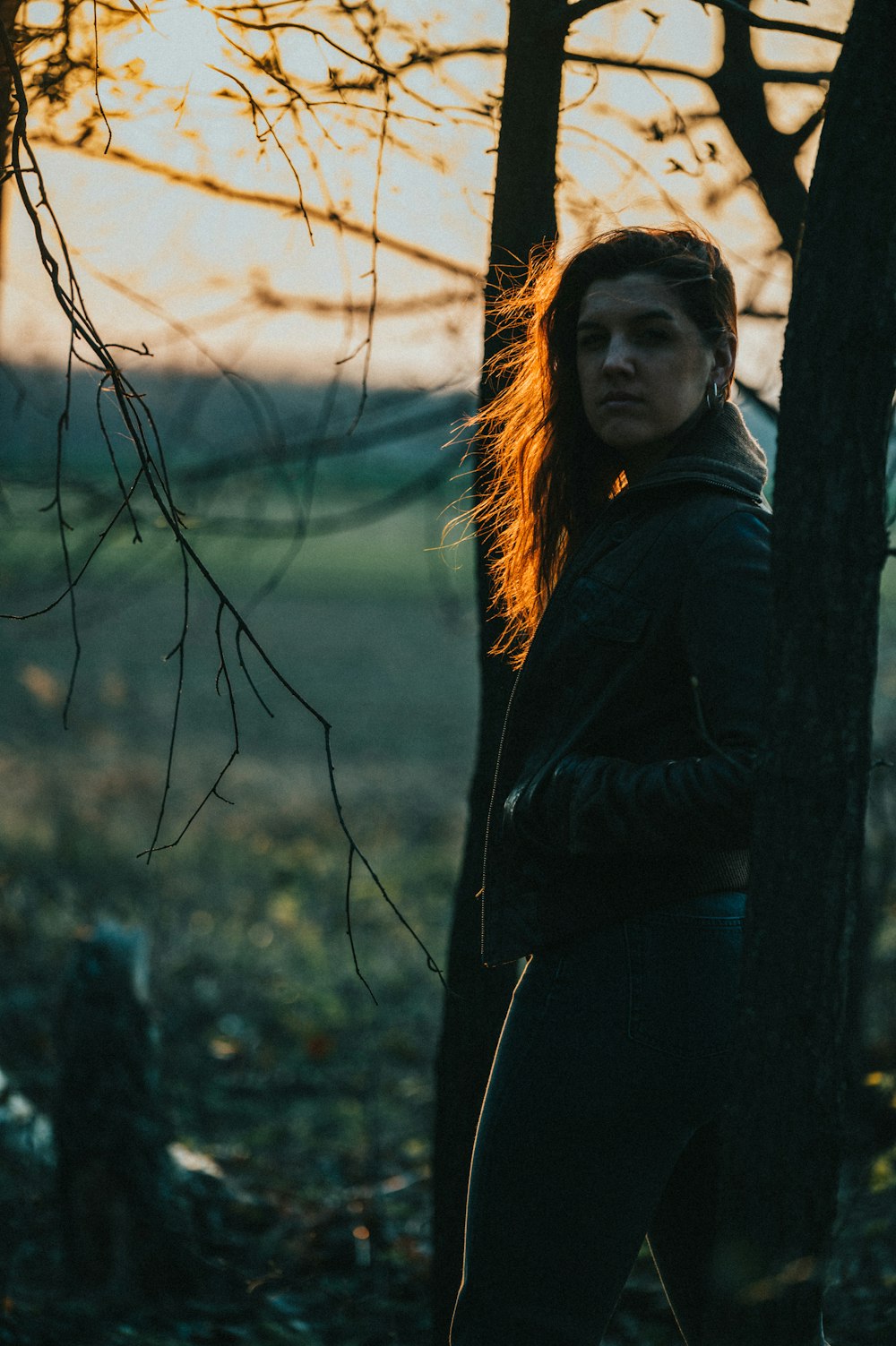 woman in black jacket standing beside brown tree during daytime