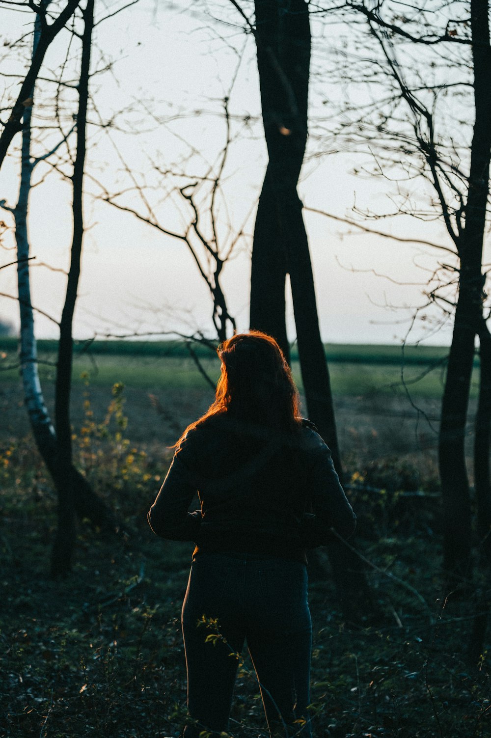 woman in black jacket standing near bare tree during daytime