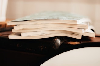 A stack of magazines is placed on a wooden surface. The image focuses on the edges of the pages, giving a sense of the texture and paper quality.