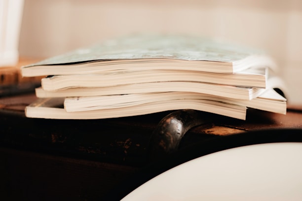 A stack of magazines is placed on a wooden surface. The image focuses on the edges of the pages, giving a sense of the texture and paper quality.