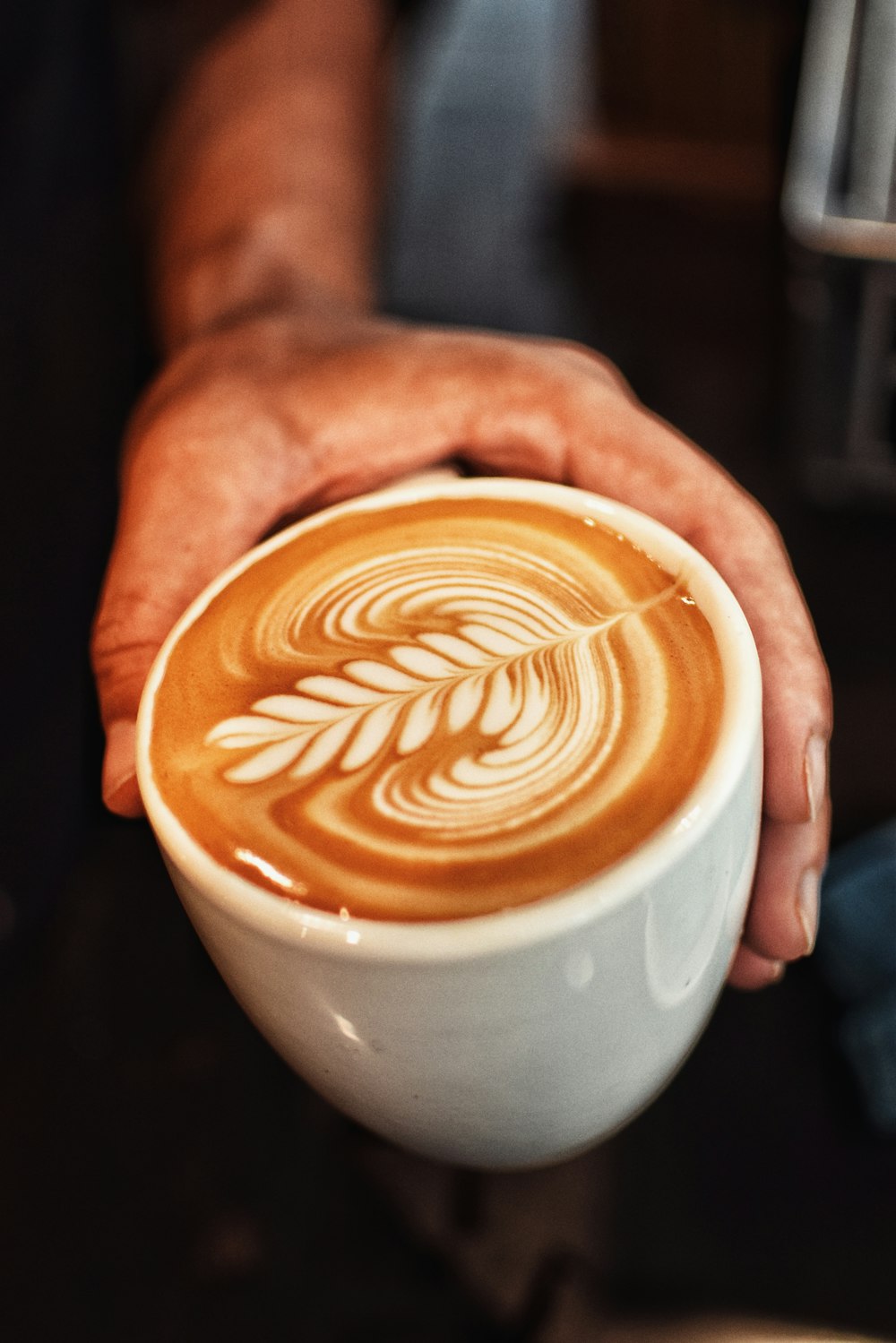 Persona che tiene la tazza di ceramica bianca con liquido marrone e bianco