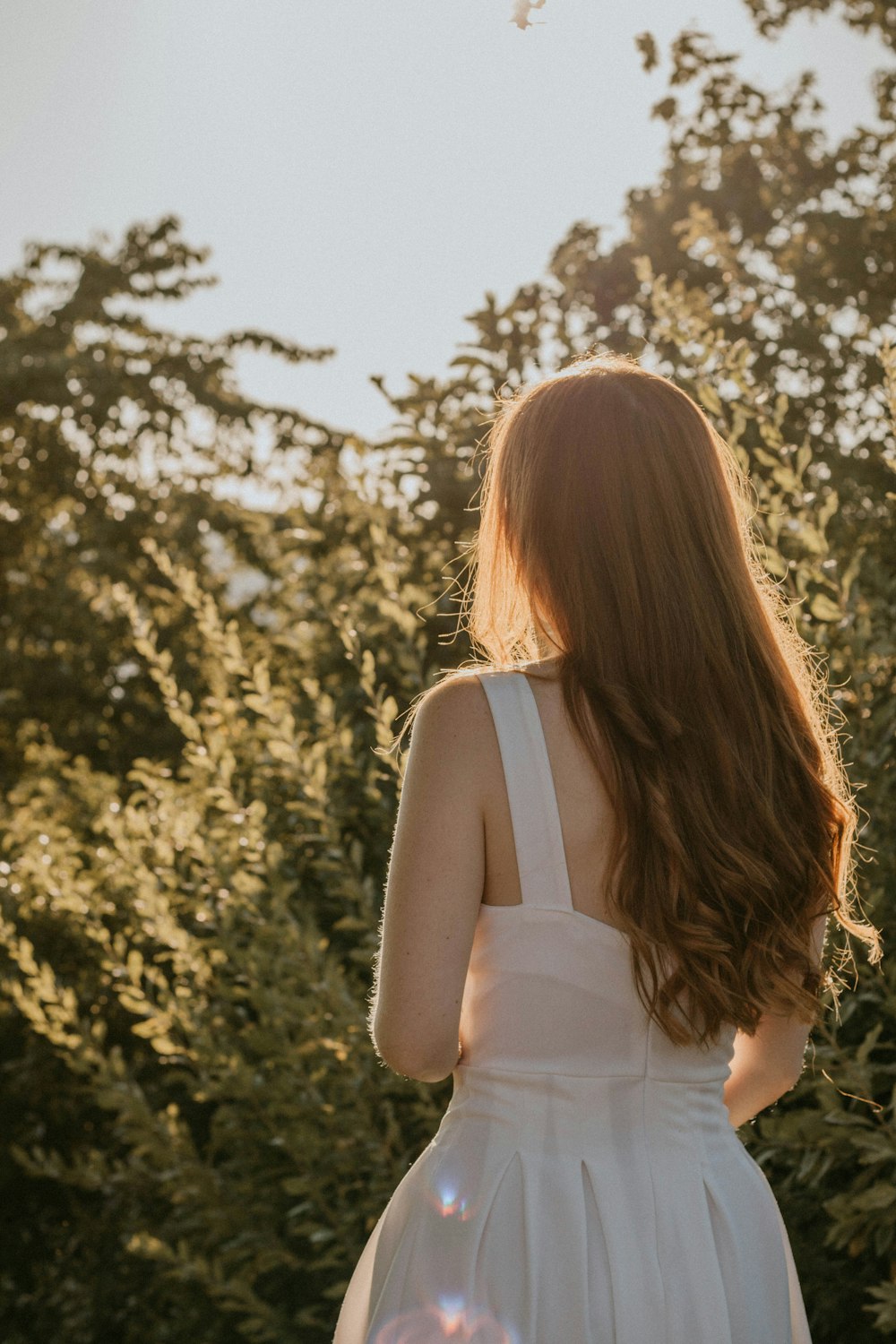 woman in white tank top standing near green trees during daytime