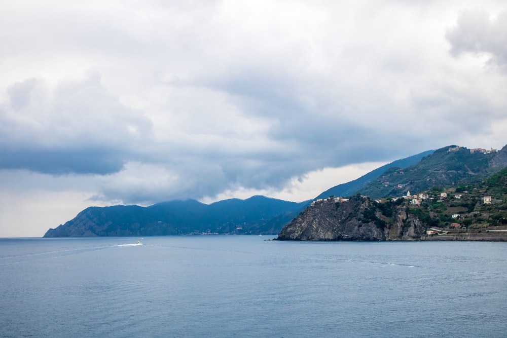 body of water near mountain under white clouds during daytime