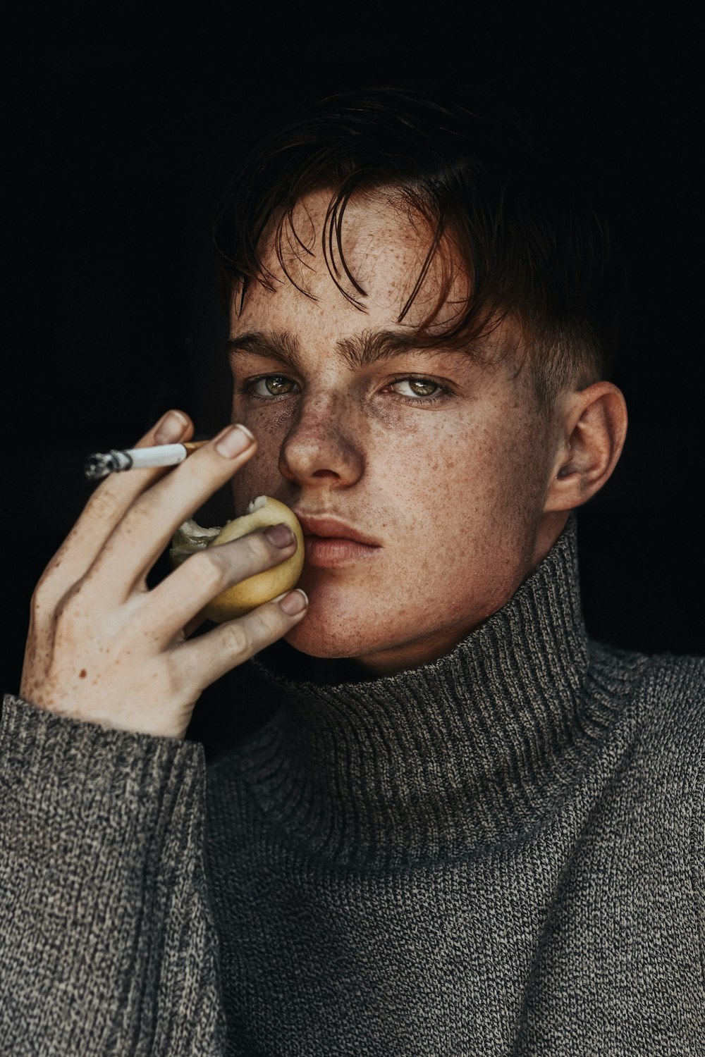 man in gray sweater holding cigarette stick