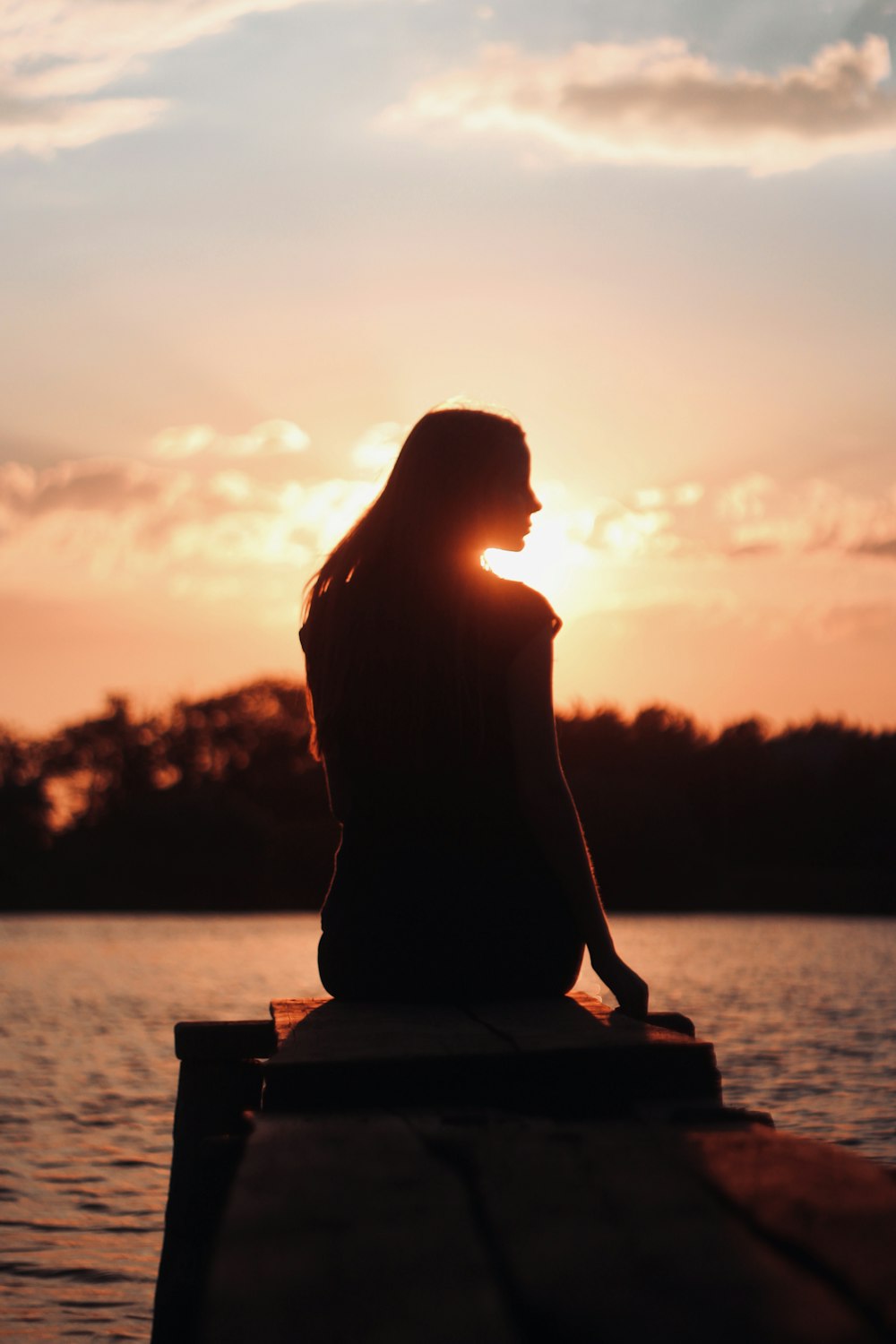 silhouette of woman sitting on brown wooden bench during sunset