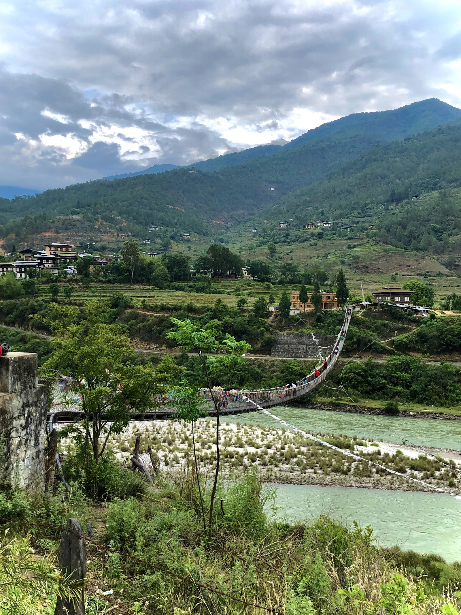 A long prayer flag footbridge over the river in the Punakha valley with terraced fields beyond