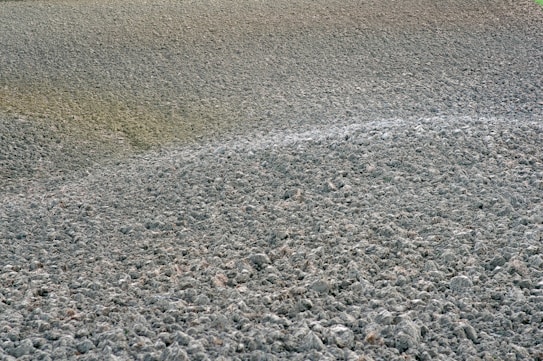A field of freshly plowed earth is visible, with rough, clumped soil forming uneven textures across the expanse. The soil appears dry and is spread across rolling, undulating patterns, suggesting recent agricultural activity.