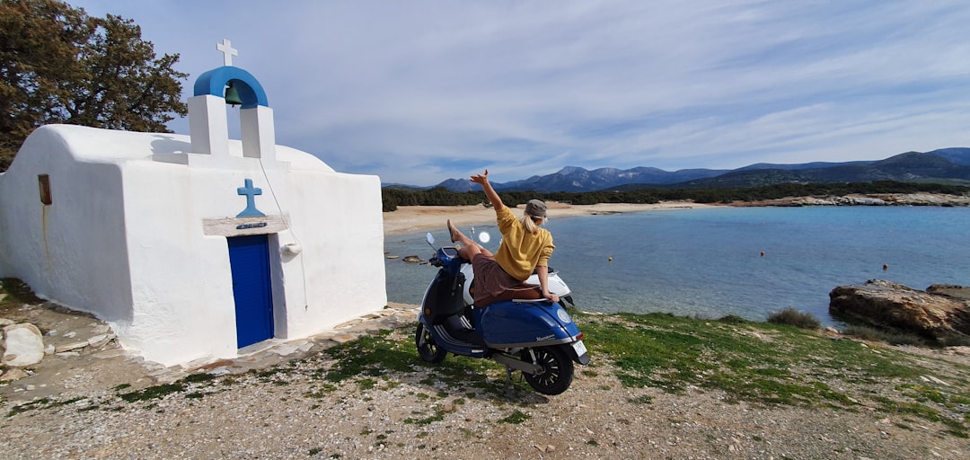 woman in brown jacket riding blue motor scooter on beach during daytime, Enjoy the view and temperatures in Greece!<p></figure>A girl sitting on her electric scooter Kumpan 1954 Ri. 