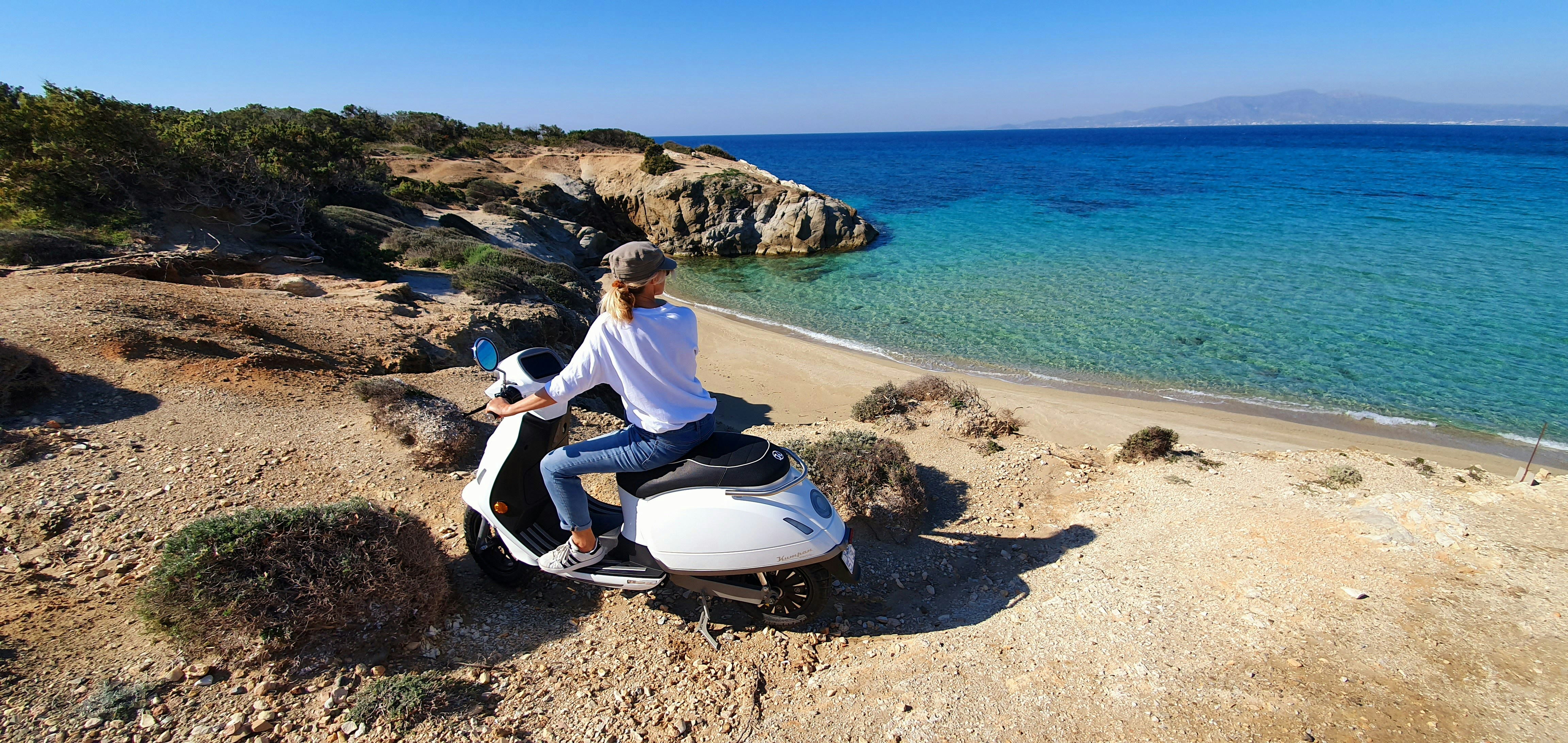 hombre con camisa blanca y pantalones azules sentado en scooter de motor blanco y negro en la playa