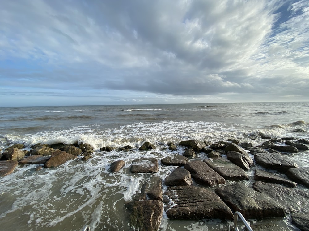 brown rocks on sea shore under white clouds and blue sky during daytime