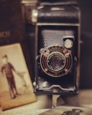A vintage Kodak camera is positioned prominently, surrounded by old sepia-toned photographs and an open book. The camera features intricate details on its lens, giving a sense of nostalgia and history.