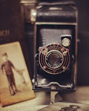 A vintage Kodak camera is positioned prominently, surrounded by old sepia-toned photographs and an open book. The camera features intricate details on its lens, giving a sense of nostalgia and history.
