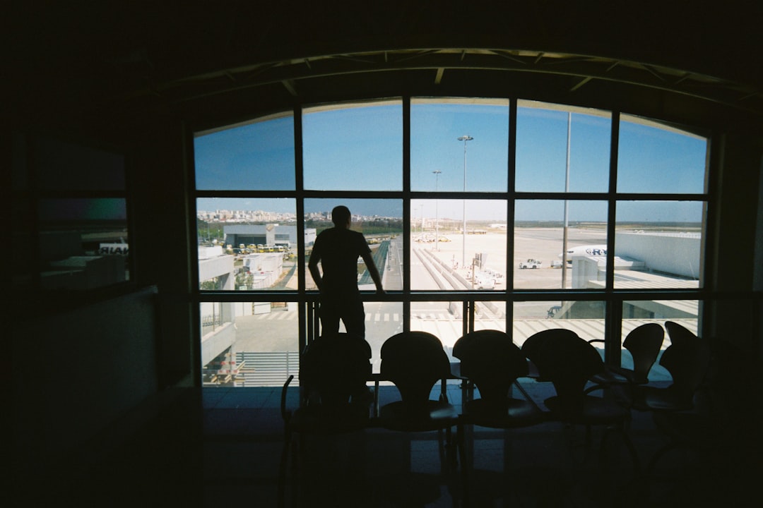silhouette of man standing near glass window, A man looking out of a window of an airport terminal lounge at the runways