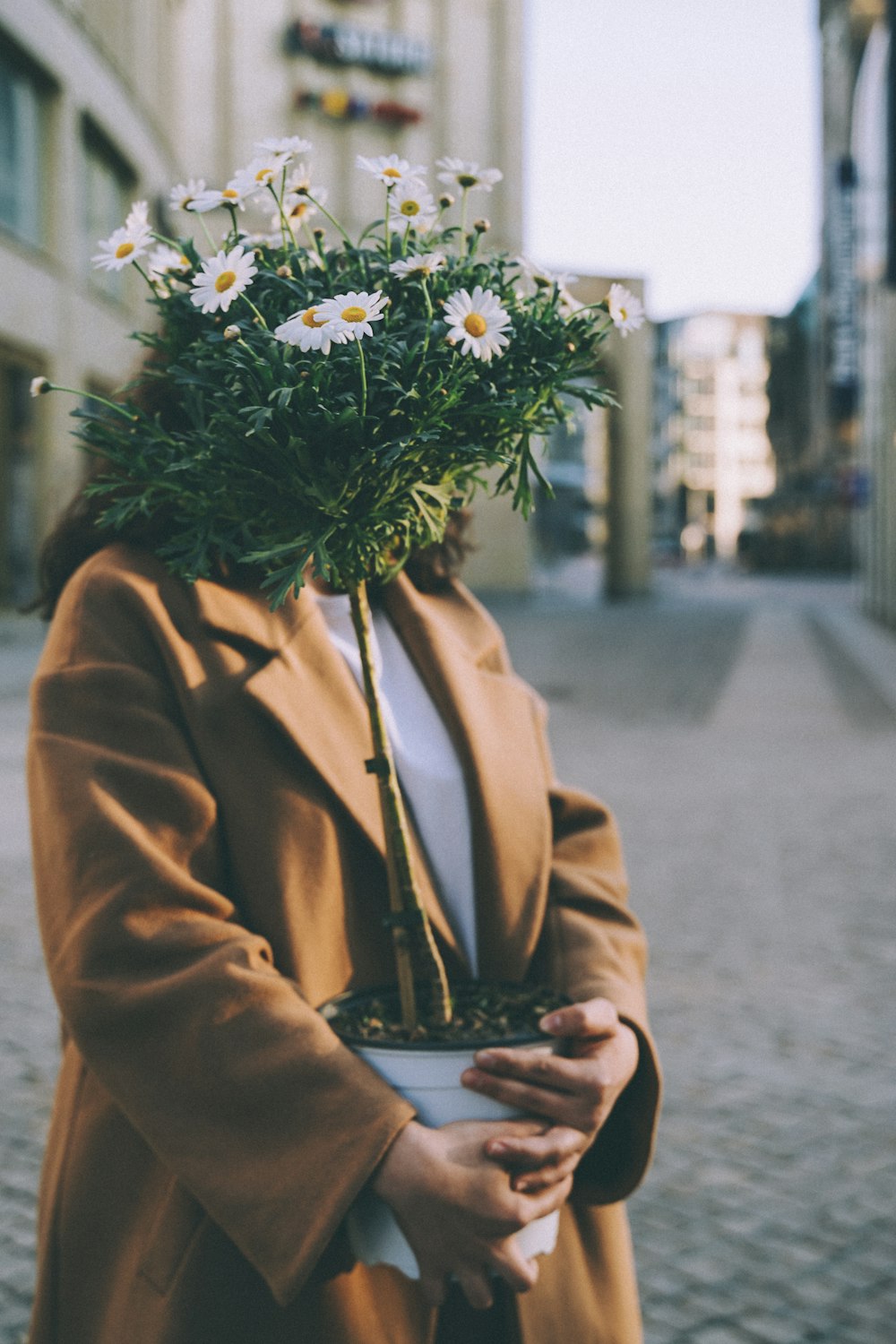person in brown coat holding white flowers