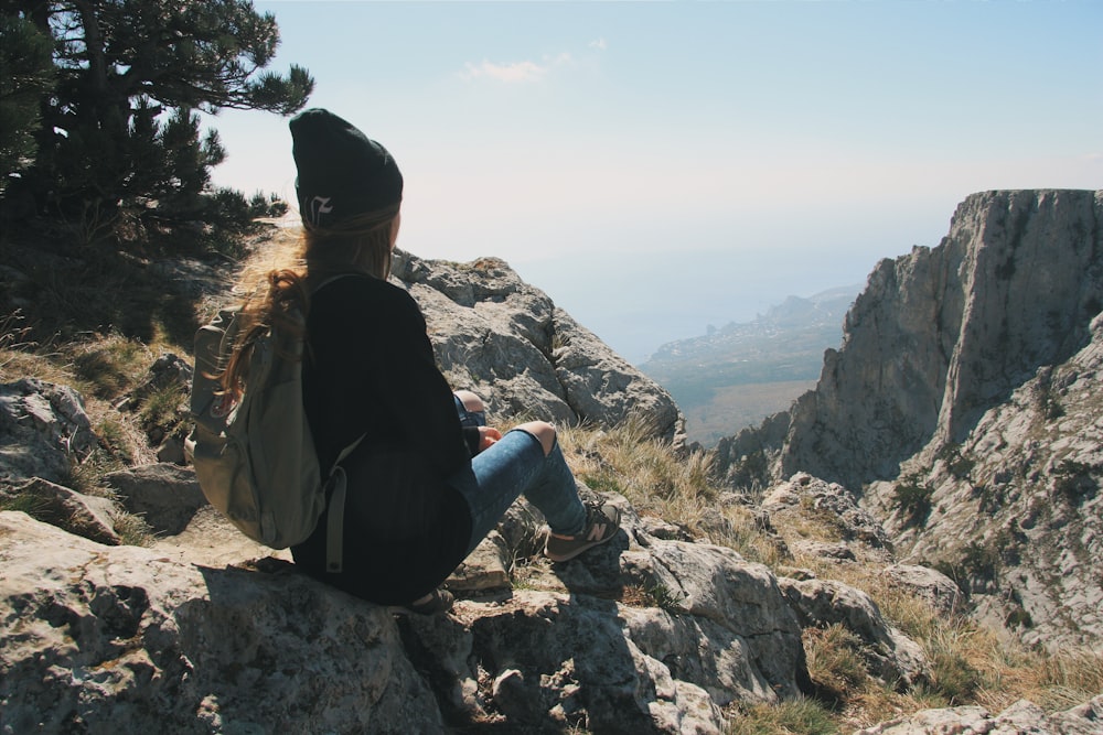 man in black jacket and blue denim jeans sitting on rock during daytime