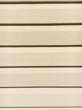Horizontal beige siding panels with a textured surface. The panels are evenly spaced and aligned, providing a uniform appearance.
