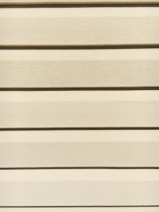 Horizontal beige siding panels with a textured surface. The panels are evenly spaced and aligned, providing a uniform appearance.