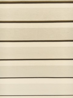 Horizontal beige siding panels with a textured surface. The panels are evenly spaced and aligned, providing a uniform appearance.