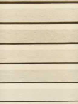 Horizontal beige siding panels with a textured surface. The panels are evenly spaced and aligned, providing a uniform appearance.