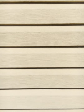 Horizontal beige siding panels with a textured surface. The panels are evenly spaced and aligned, providing a uniform appearance.