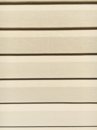Horizontal beige siding panels with a textured surface. The panels are evenly spaced and aligned, providing a uniform appearance.