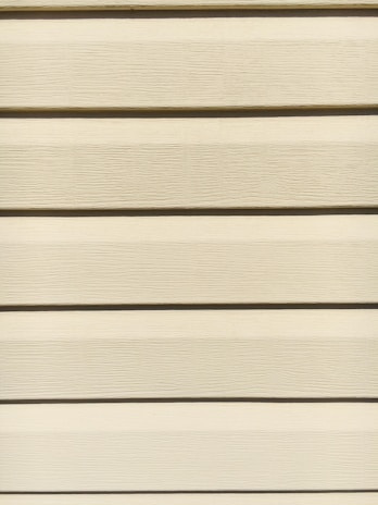 Horizontal beige siding panels with a textured surface. The panels are evenly spaced and aligned, providing a uniform appearance.