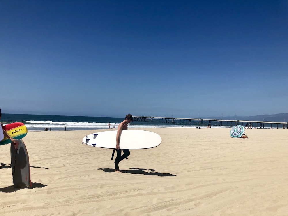 woman in white dress holding white surfboard walking on beach during daytime