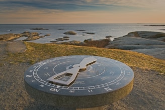 A close-up of a compass rose overlaying a lighthouse silhouette against a grey sky.