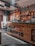 A cozy coffee shop interior featuring wooden decor, a counter with coffee brewing equipment, shelves stocked with jars and bottles, and signs displaying coffee-related messages. Ambient lighting with small string lights adds warmth to the atmosphere.
