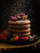 pancakes with strawberries and blueberries on black ceramic plate