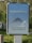 A public advertisement board with a message promoting social responsibility against COVID-19. It features the hashtag #flattenthecurve in bold white letters above a diagram illustrating a flattened curve. Below, the text 'Tous ensemble contre le COVID-19' is displayed, encouraging collective action. The board is set outdoors, surrounded by greenery.
