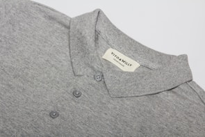 A neatly folded grey polo shirt with a collar and three buttons is displayed, featuring a label sewn inside the collar area with the brand name 'VITO & WILLY'. The fabric appears soft and finely woven, and the color is a consistent light grey.