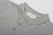 A neatly folded grey polo shirt with a collar and three buttons is displayed, featuring a label sewn inside the collar area with the brand name 'VITO & WILLY'. The fabric appears soft and finely woven, and the color is a consistent light grey.
