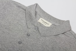 A neatly folded grey polo shirt with a collar and three buttons is displayed, featuring a label sewn inside the collar area with the brand name 'VITO & WILLY'. The fabric appears soft and finely woven, and the color is a consistent light grey.
