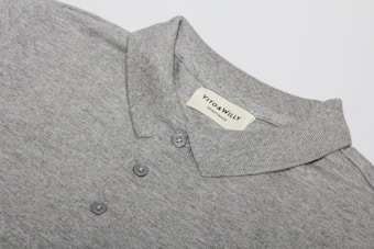 A neatly folded grey polo shirt with a collar and three buttons is displayed, featuring a label sewn inside the collar area with the brand name 'VITO & WILLY'. The fabric appears soft and finely woven, and the color is a consistent light grey.