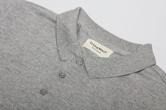 A neatly folded grey polo shirt with a collar and three buttons is displayed, featuring a label sewn inside the collar area with the brand name 'VITO & WILLY'. The fabric appears soft and finely woven, and the color is a consistent light grey.