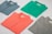 Four folded polo shirts in different colors are arranged symmetrically on a flat surface. The colors include blue, green, coral, and gray. Each shirt has a tag visible near the collar.